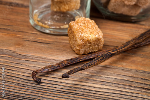 Vanilla beans with brown sugar pieces on a wooden background. Macro photography of spices.