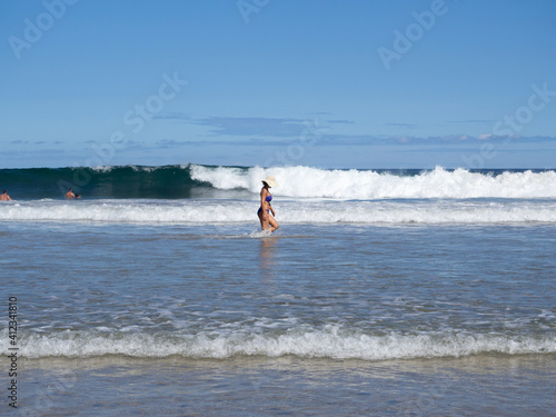 Mujer con sombrero y biquini caminando entre las olas de la playa de la Ensenada de Fuentes en Cantabria, verano de 2020

