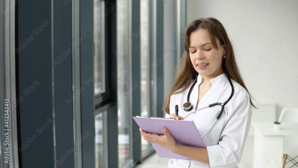 Young caucasian woman doctor wearing white medical coat and stethoscope with documents in her hands looking at camera. Smiling female physician posing in hospital office Young caucasian woman doctor wearing white medical coat and stethoscope with documents in her hands looking at camera. Smiling female physician posing in hospital office