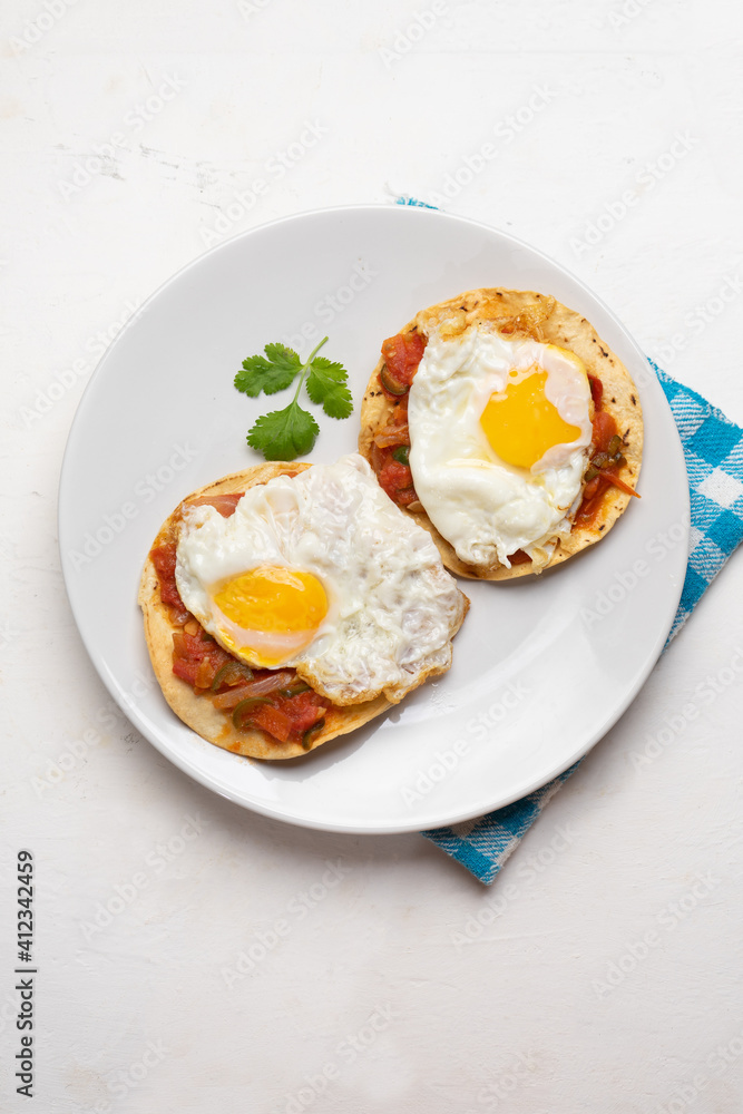 Fried eggs with sauce and tortilla called rancheros for  breakfast on white background. Mexican food