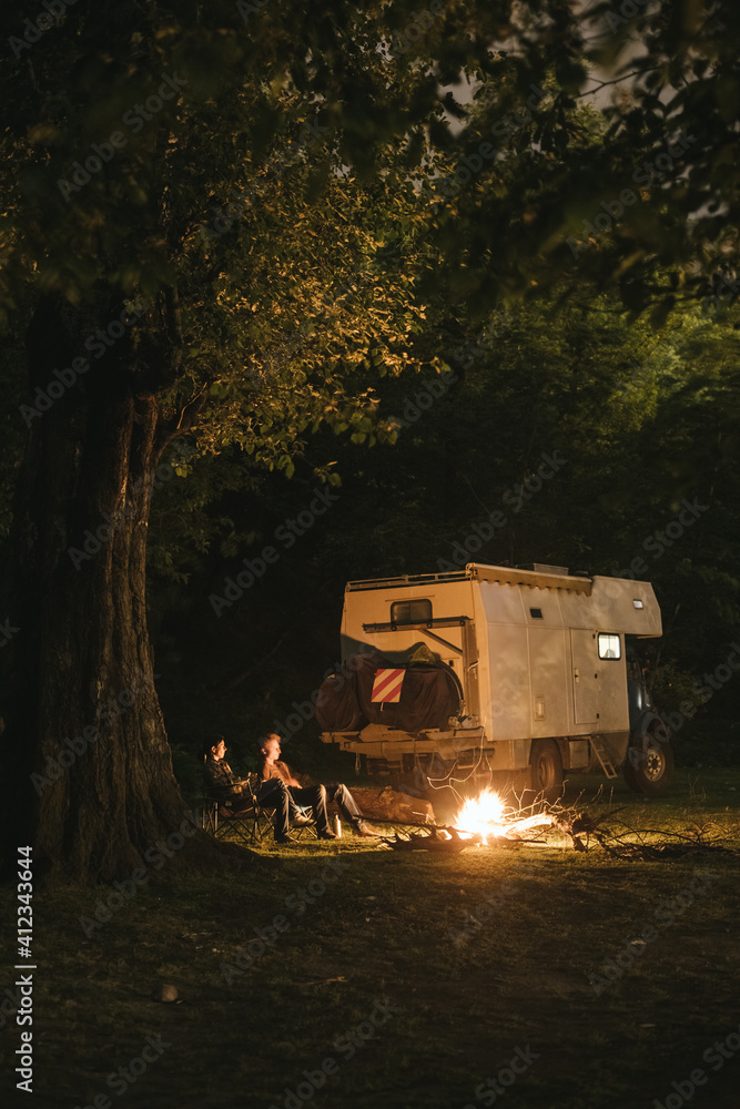 couple with campingtruck enjoying bonfire at night in the forest couple with campingtruck enjoying bonfire at night in the forest