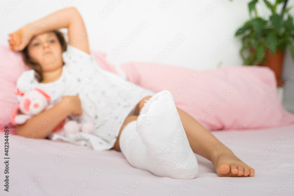 A sad teenage girl lies on a bed with a cast on her leg, with a fractured ankle and crutches. Broken leg in a child.Close up A sad teenage girl lies on a bed with a cast on her leg, with a fractured ankle and crutches. Broken leg in a child.Close up