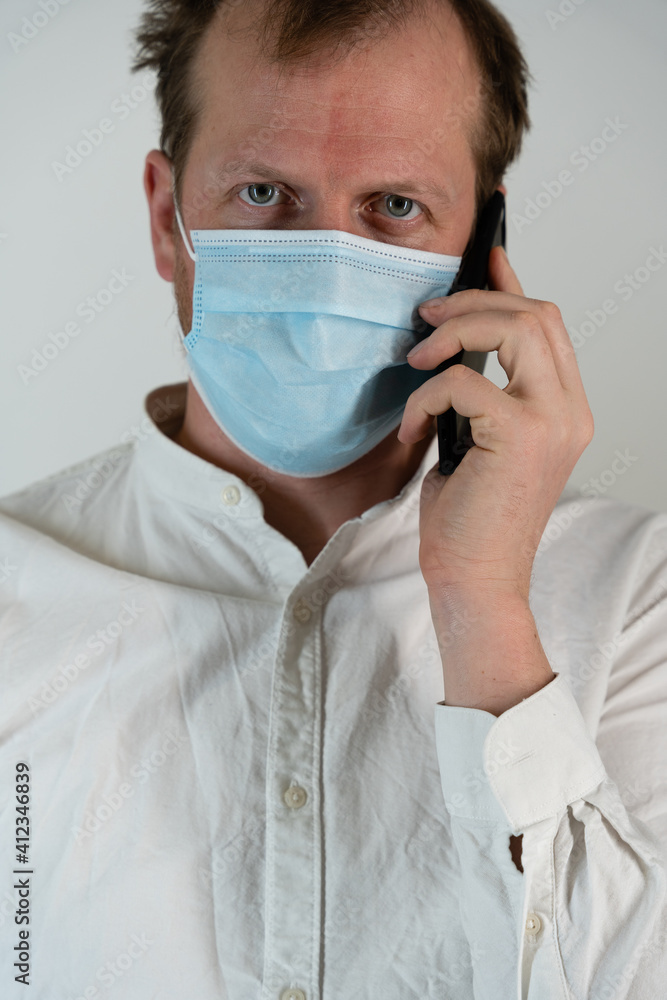 Portrait of a straight man with a white shirt with curly hair and a direct firm look and face mask to protect against covid19, he has a black mobile phone Portrait of a straight man with a white shirt with curly hair and a direct firm look and face mask to protect against covid19, he has a black mobile phone