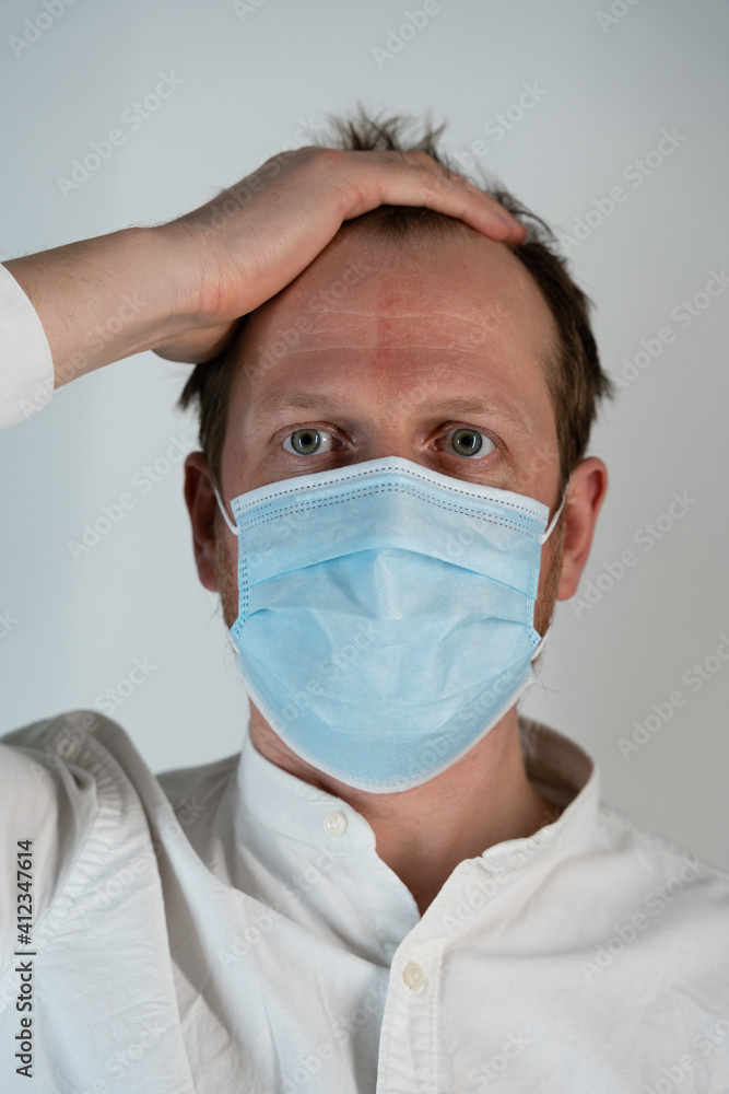 Portrait of a straight man in a white shirt with curly hair and a straight tight look and face mask to protect against covid19, he has caught his head Portrait of a straight man in a white shirt with curly hair and a straight tight look and face mask to protect against covid19, he has caught his head