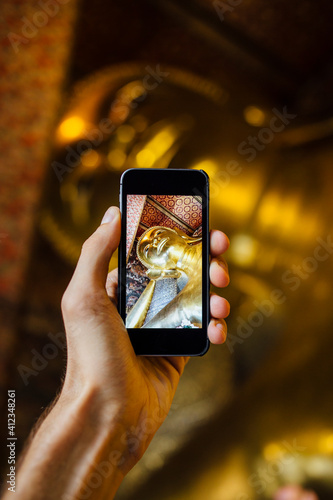 Man taking photo with phone of Reclining Buddha in Wat Pho Temple photo