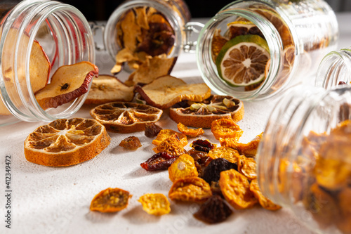 side view of dried fruit, apple, lemon, tangerine, grapes, golden berries and glass jars on a white background