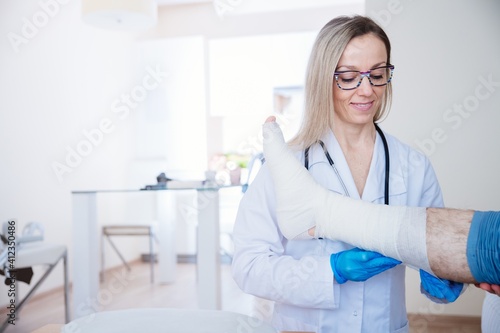 Smiling proffesional nurse in glasses bandages the leg. Medical care.