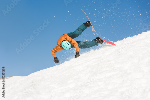 Male snowboarder falling down while riding downhill snow slope photo