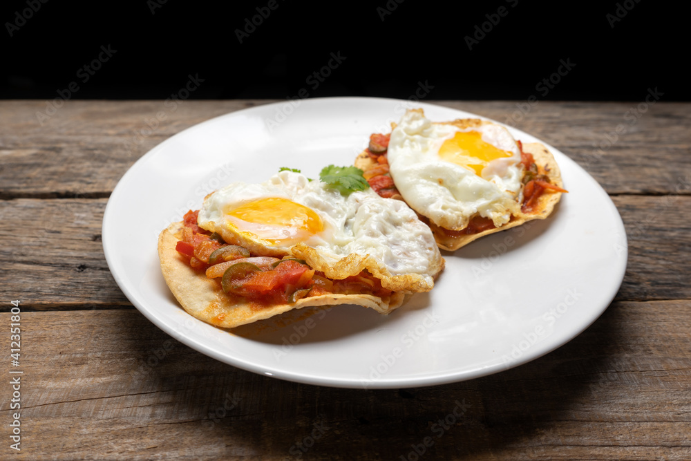 Fried eggs with sauce and tortilla called rancheros for  breakfast on wooden background. Mexican food