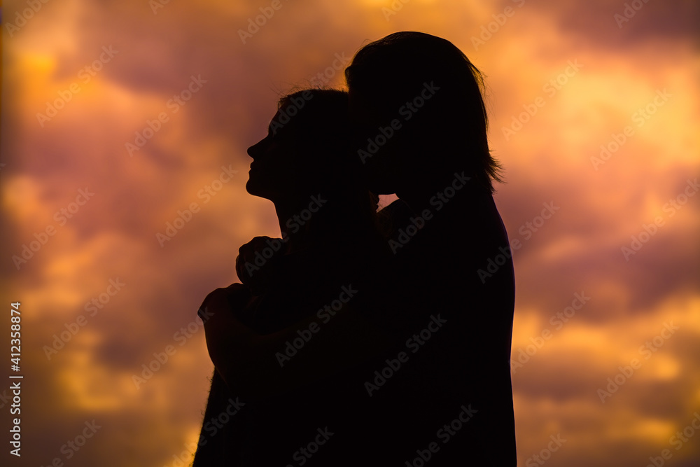The silhouette of a young couple loving each other on the background of the sunset. A couple in love at sunset with a copy of the text space.