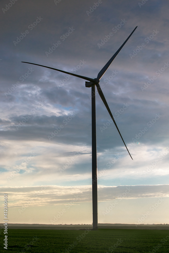 Obraz premium silhouette wind turbine offshore windmill made of iron with blades on field against a blue sky with clouds on sunset, alternative electricity preserving nature.