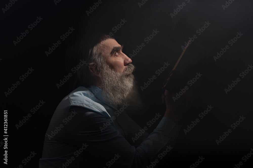 A senior man standing in dark smoky background light ray from above. Prayer gesture A senior man standing in dark smoky background light ray from above. Prayer gesture