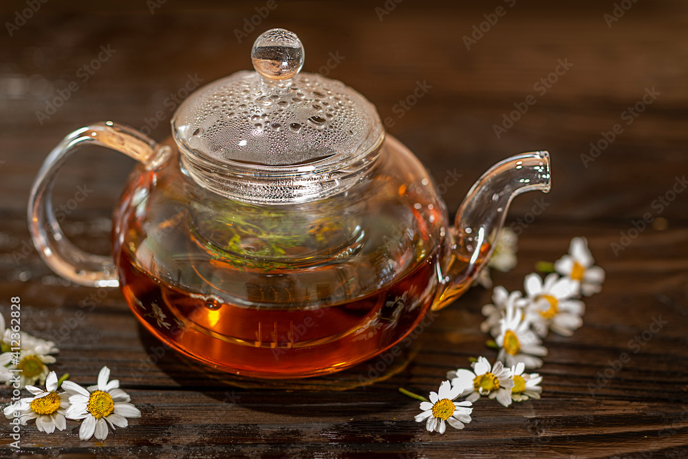 Steaming glass teapot with chamomile tea on a wet wooden table. Steaming glass teapot with chamomile tea on a wet wooden table.