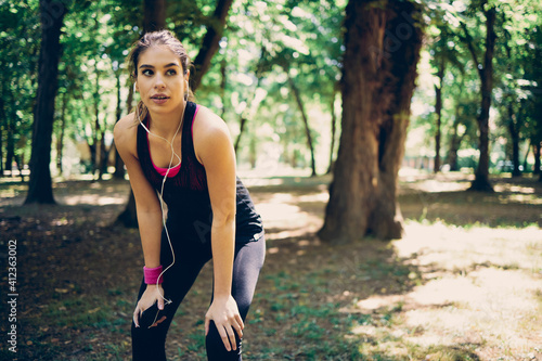 Young attractive fit caucasian sportswoman standing in nature and using smart phone to search music for running.