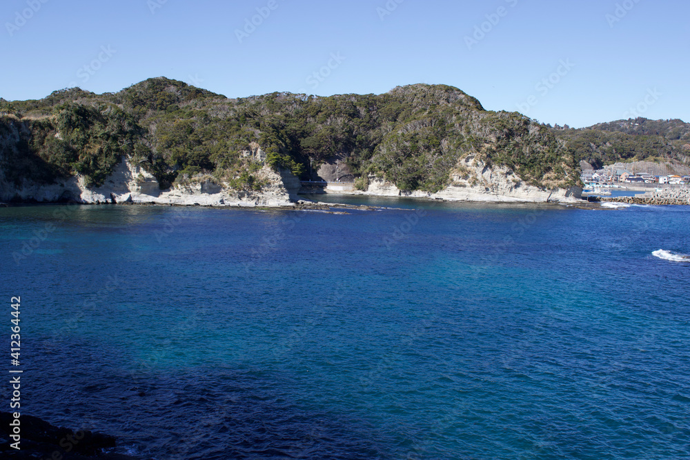 Katsuura Bay in Chiba Japan view, the ocean is a stunning deep blue color and the day is clear. It is a very idyllic scene. High cliffs and green hills.