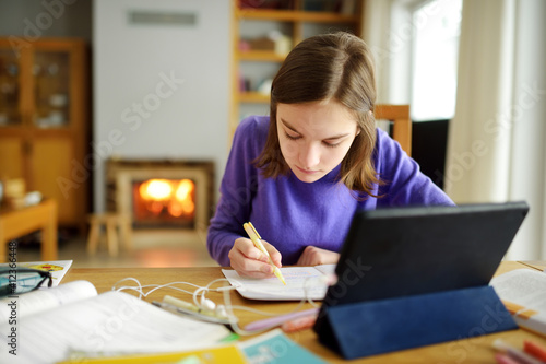 Preteen schoolgirl doing her homework with digital tablet at home. Child using gadgets to study. Education and distance learning for kids. Homeschooling during quarantine.
