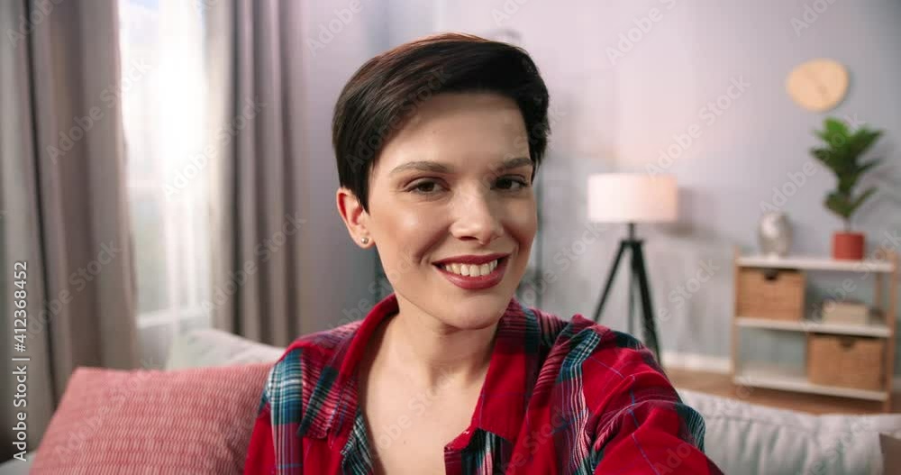 Head shot close up portrait happy healthy caucasian brunette woman sitting on comfortable couch at home. Smiling pleasant girl looking at camera, posing for photo in modern living room Head shot close up portrait happy healthy caucasian brunette woman sitting on comfortable couch at home. Smiling pleasant girl looking at camera, posing for photo in modern living room