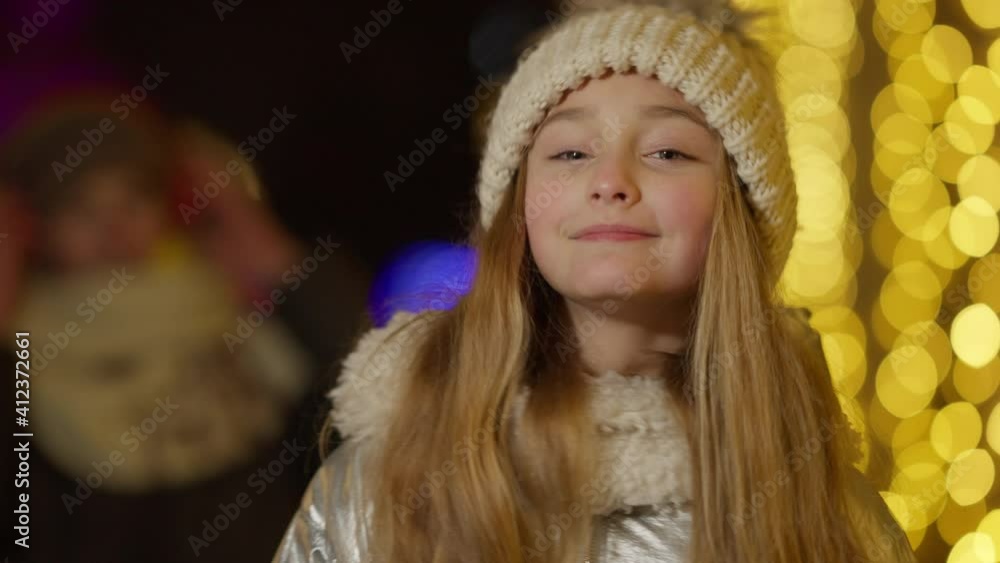 Cute Caucasian girl grimacing in slow motion as blurred positive boy in headphones dancing at background. Charming children celebrating Christmas outdoors in city. Joy and leisure. Cute Caucasian girl grimacing in slow motion as blurred positive boy in headphones dancing at background. Charming children celebrating Christmas outdoors in city. Joy and leisure.