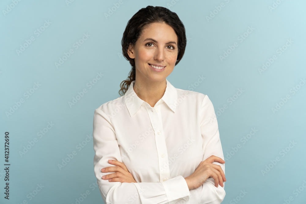 Confident businesswoman or office employee, smiling, looking at camera posing isolated on blue background. Studio portrait of successful friendly female lawyer in blouse, crossed arms. Confident businesswoman or office employee, smiling, looking at camera posing isolated on blue background. Studio portrait of successful friendly female lawyer in blouse, crossed arms.