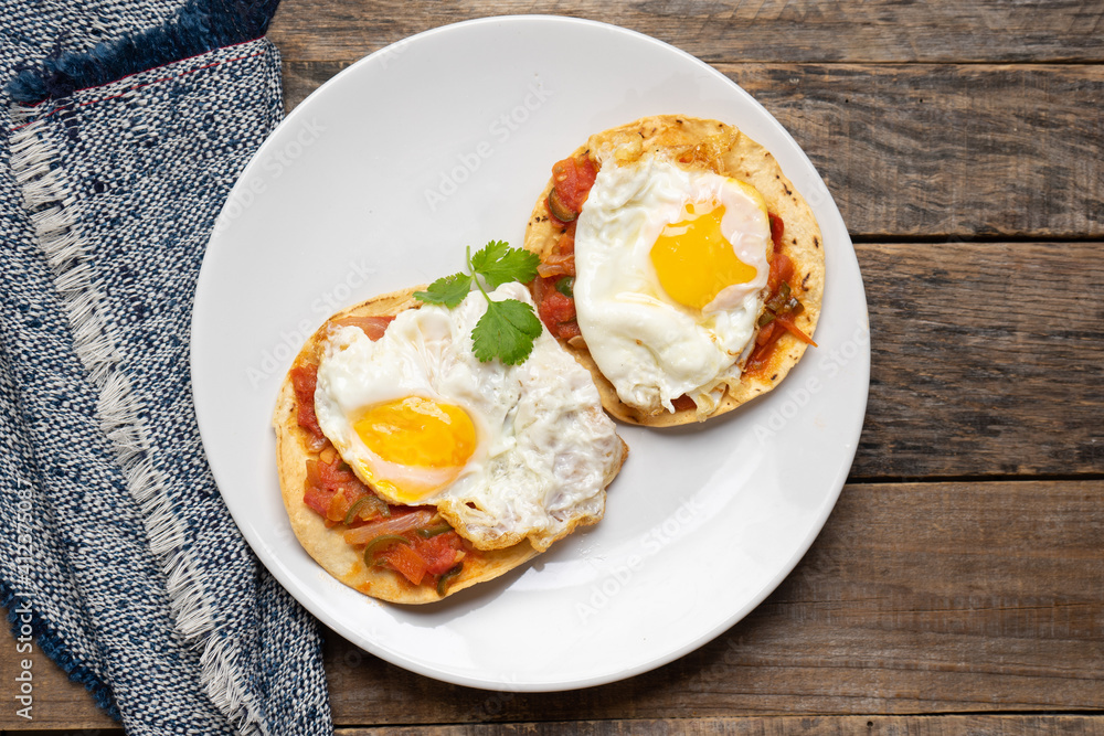 Fried eggs with sauce and tortilla called rancheros for breakfast on wooden background. Mexican food Fried eggs with sauce and tortilla called rancheros for breakfast on wooden background. Mexican food
