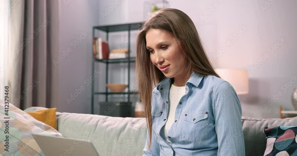 Smiling millennial girl relax on couch and using modern laptop while browsing unlimited wireless internet. Happy young woman freelancer working on computer while texting from home. Technology concept Smiling millennial girl relax on couch and using modern laptop while browsing unlimited wireless internet. Happy young woman freelancer working on computer while texting from home. Technology concept