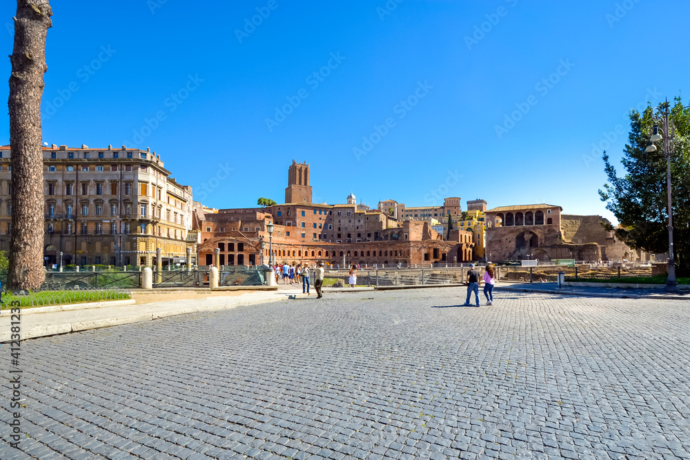Tourists enjoy a sunny day sightseeing near the ruins of Trajan's Market in the historic center of Rome, Italy