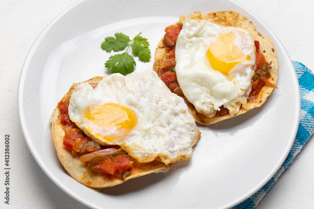 Fried eggs with sauce and tortilla called rancheros for  breakfast on white background. Mexican food