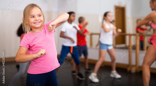 Portrait of cheerful preteen girl practicing dance movements with group of children in choreography class
