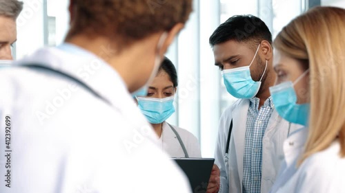 Multiracial team of doctors discussing a patient standing grouped in the foyer looking at a tablet, close up. Diverse multiracial medical team consulting on a patient records grouped around a tablet photo