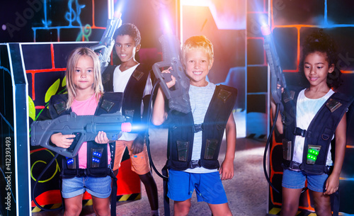 Modern teenage girl and boys with laser guns playing laser tag on dark arena. High quality photo