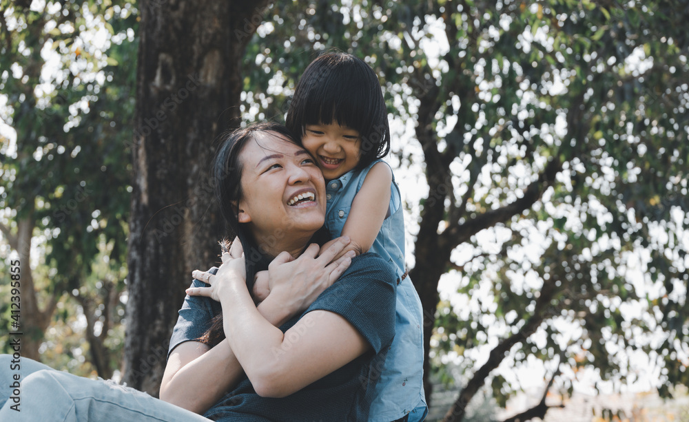 Asian little daughter hug her mom with smile in the park. Concept for family relationship and relaxing time. Asian little daughter hug her mom with smile in the park. Concept for family relationship and relaxing time.