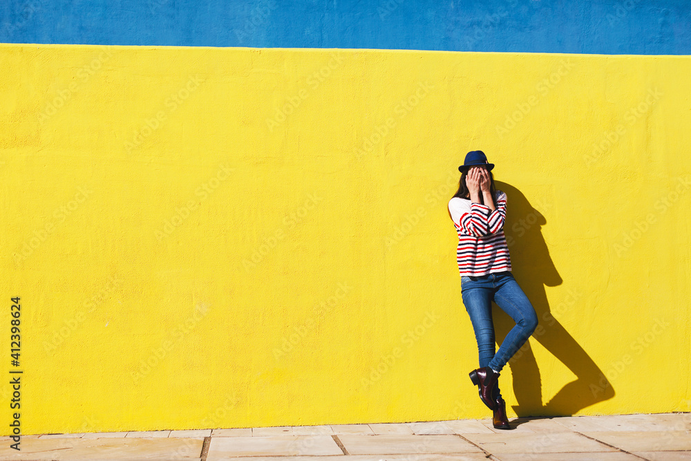Young woman hiding her face in front of yellow background. Young woman hiding her face in front of yellow background.