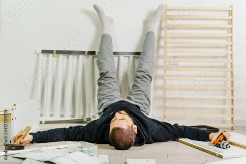 Fotografie One man lying on the floor at home exhausted during self assembly project trying