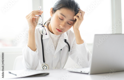 Portrait of young asian female doctor sitting on the desk with tired expression