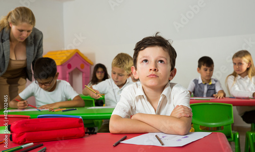 Portrait of bored schoolboy sitting in classroom with classmates and teacher