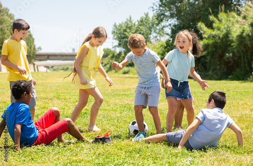 Group of happy schoolchildren playing football together in park