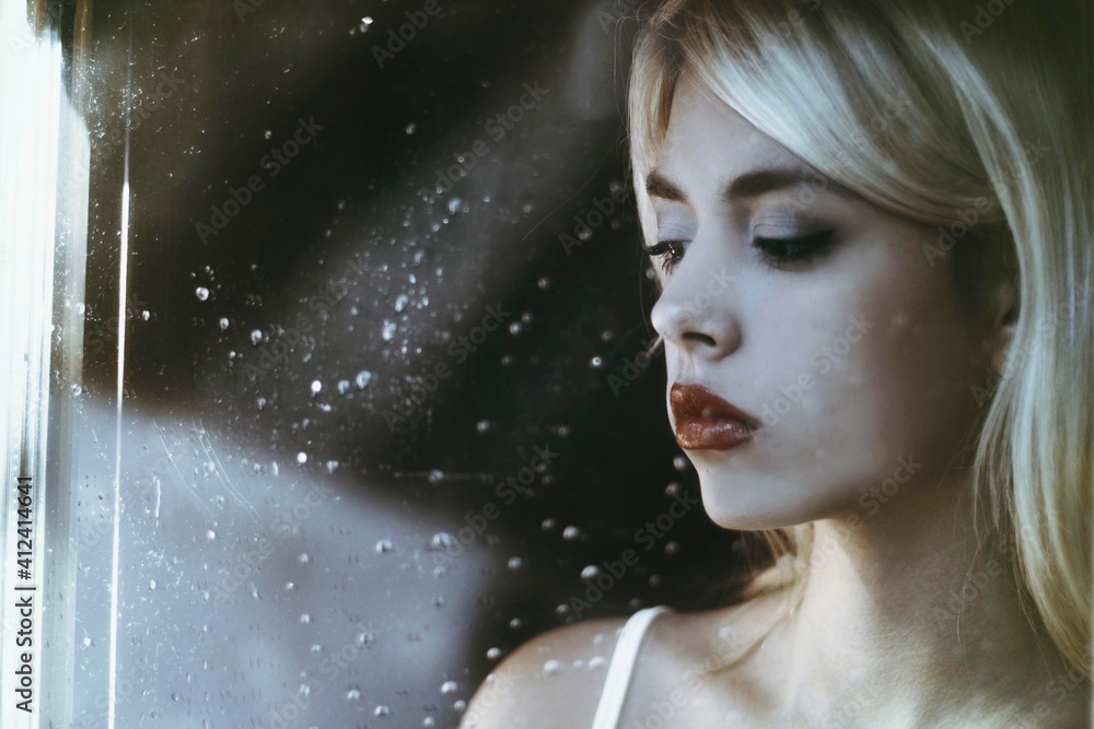 Beautiful girl standing at the window watching the rain Beautiful girl standing at the window watching the rain