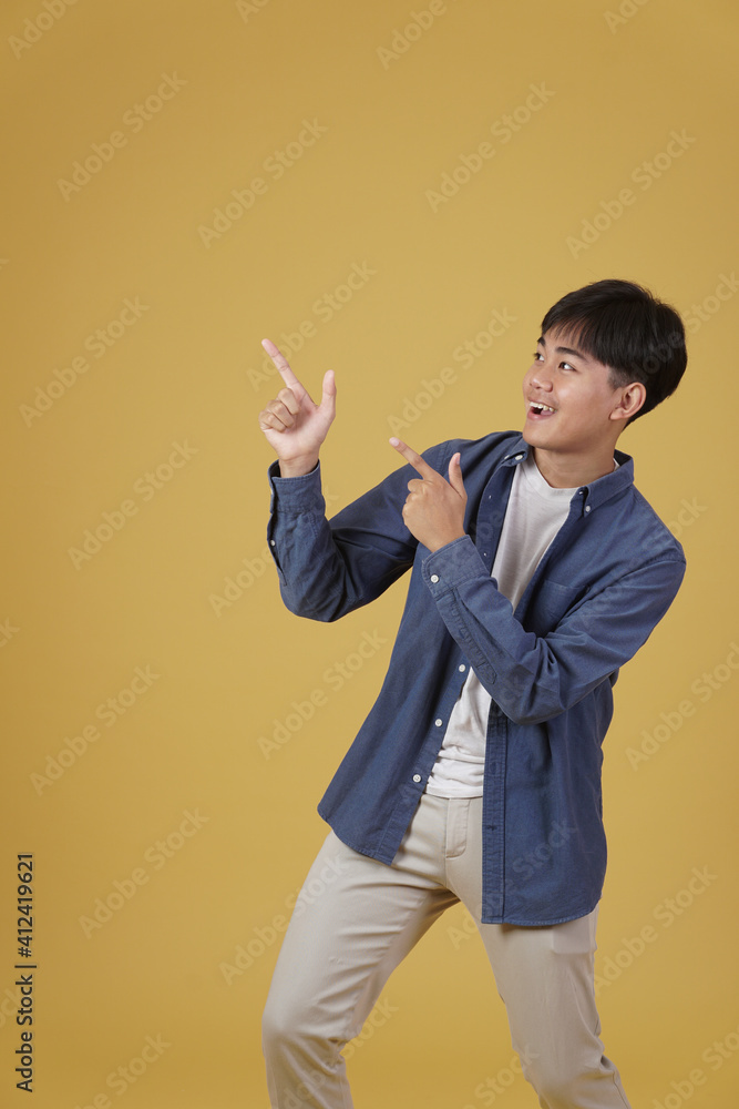 portrait of happy handsome young asian man dressed casually pointing fingers at copyspace isolated on yellow background portrait of happy handsome young asian man dressed casually pointing fingers at copyspace isolated on yellow background