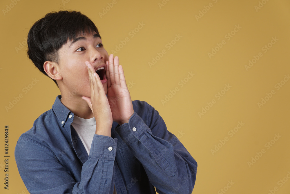 portrait of excited young asian man dressed casually with shouting announcing holding hands near mouth isolated on yellow background portrait of excited young asian man dressed casually with shouting announcing holding hands near mouth isolated on yellow background