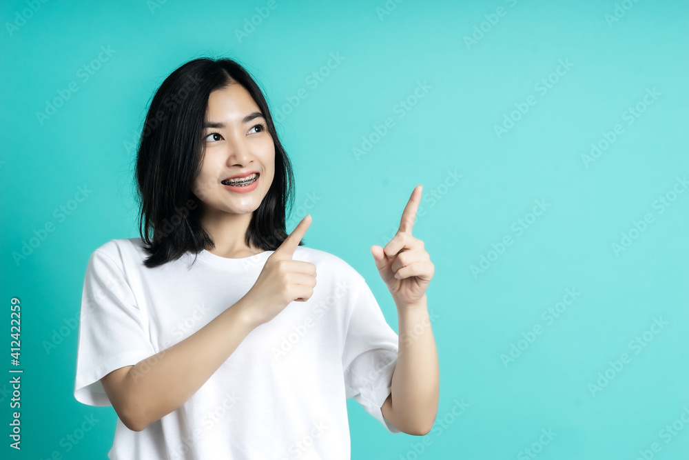 Young elegant Asian woman smiling and pointing to empty copy space isolated on blue background Young elegant Asian woman smiling and pointing to empty copy space isolated on blue background