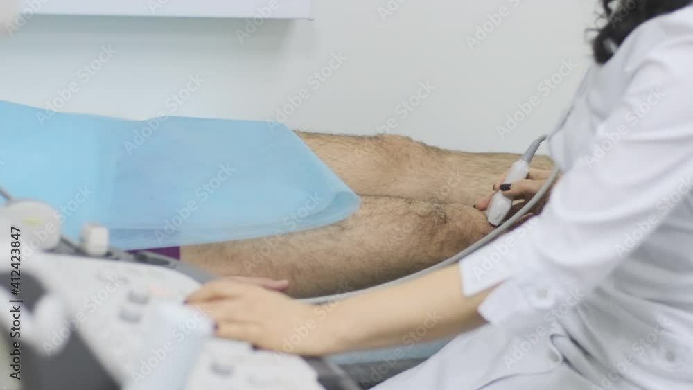 Woman doctor hands examines young man patient knee-joint using ultrasound sensor device, sonography. Doctor runs ultrasound sensor over patient's leg, knee. Woman doctor hands examines young man patient knee-joint using ultrasound sensor device, sonography. Doctor runs ultrasound sensor over patient's leg, knee.