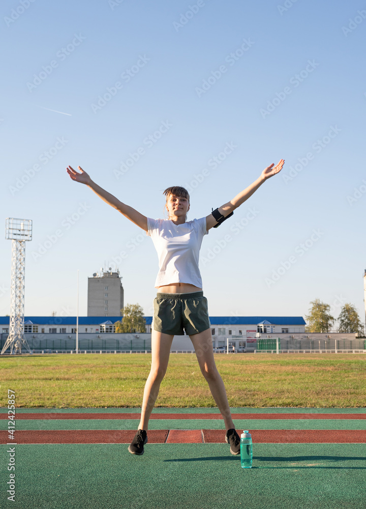 Teenager girl working out at the stadium doing jumping jacks