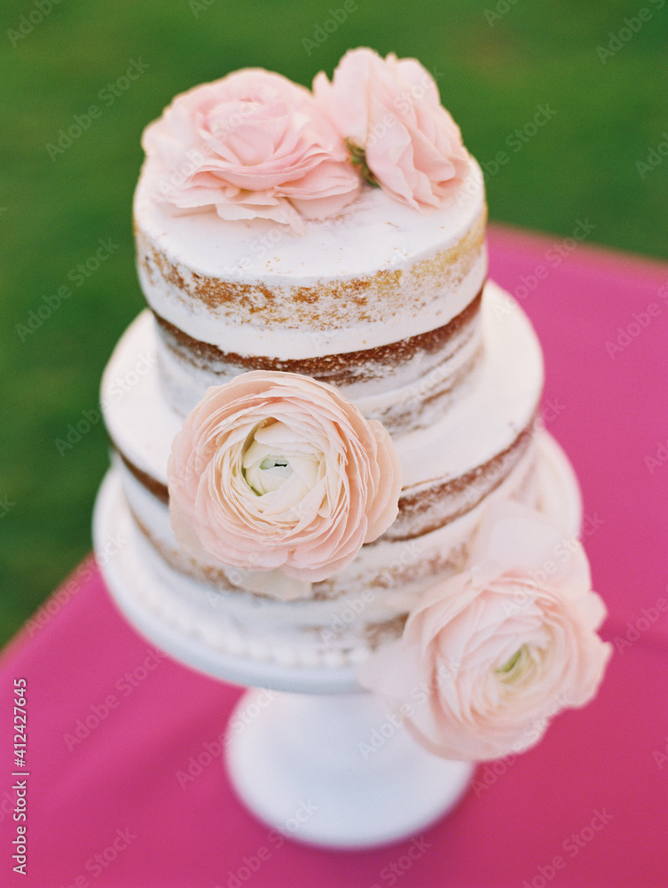 pretty wedding cake with pink flowers and tan layers on pink table pretty wedding cake with pink flowers and tan layers on pink table