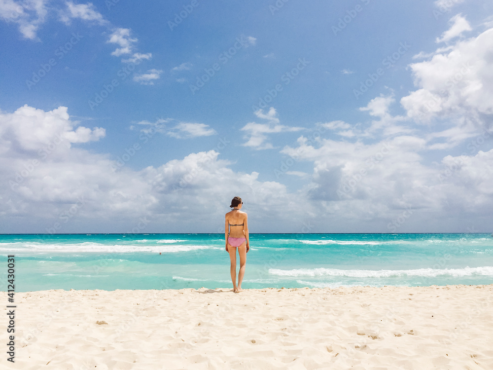 Woman in bikini standing on beach, looking at the ocean Woman in bikini standing on beach, looking at the ocean