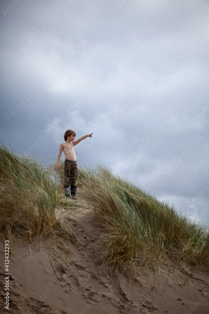 Boy on sand dune points to something unseen Boy on sand dune points to something unseen