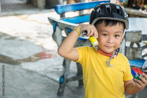 Happy kid Asian boy having fun on road ride bicycle in city. Active little child smiling while wearing helmet for bike sport outside. Young small biker playing cycle in park. Safety exercise concept.