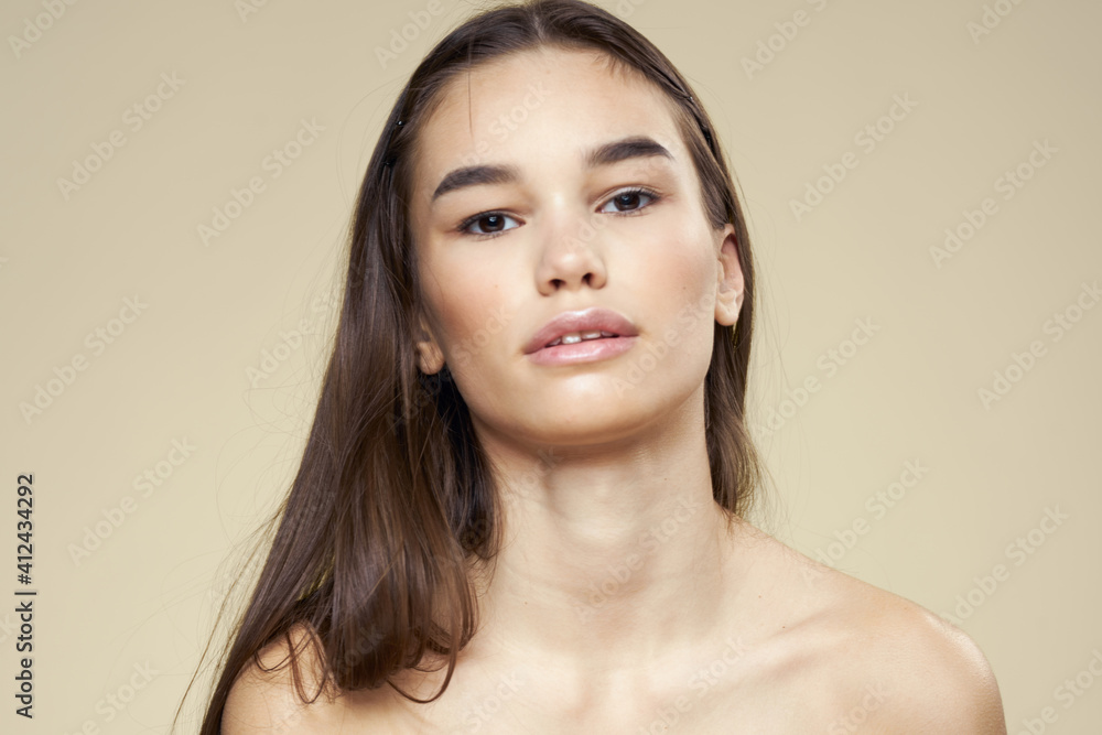 Brunette with bare shoulders close-up long hair beige background clean skin Brunette with bare shoulders close-up long hair beige background clean skin