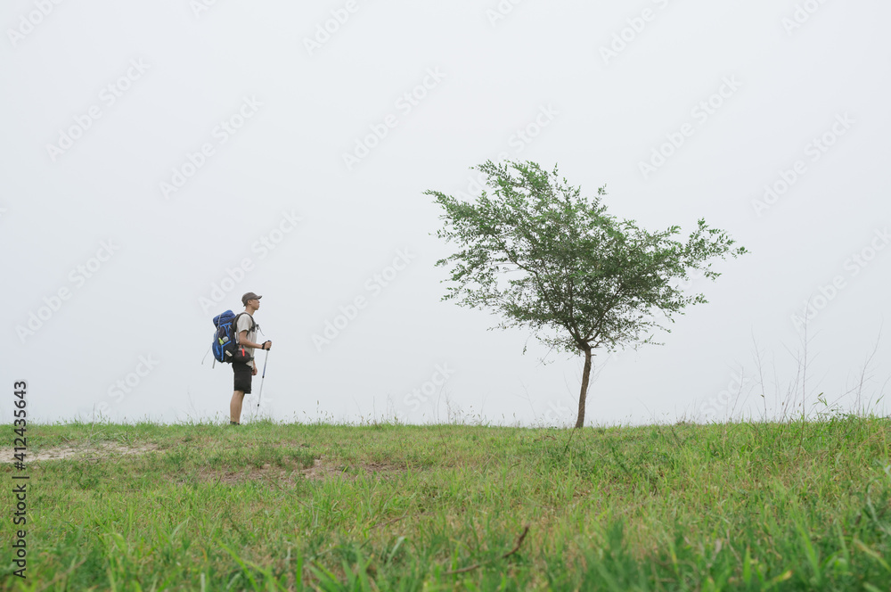 A Chinese young man hiking on grassland and looking at a tree,Beijing,China A Chinese young man hiking on grassland and looking at a tree,Beijing,China