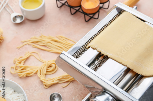 Pasta machine with dough and ingredients on color background