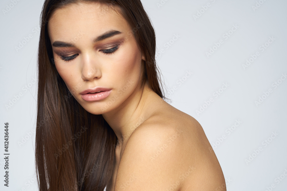 Pretty brunette naked shoulders long hair close-up light background Pretty brunette naked shoulders long hair close-up light background